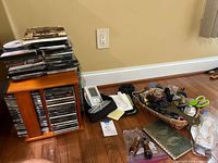 Wide shot showing wooden swivel CD rack with stacked CDs, Microlife blood pressure cuff and monitor, basket with assorted locks and cords, scissors, and other small items.