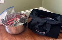 Lobster eating tools including red-handled seafood crackers and forks in plastic bag, large stainless steel mixing bowl and black Craftsman carry bag