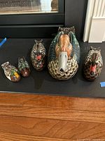 Front view of five colorfully painted wooden duck decoys of varying sizes from smallest to largest on a dark surface