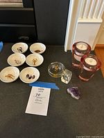 Overview of all lot items displayed on black surface: six finger bowls with sea creature images, two pink glass votive candle holders, two glass paperweights (Warwick Castle and fairy), and a purple rock fragment.