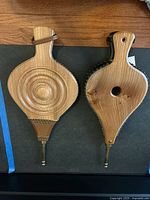 Two brass, leather, wood fireplace bellows laid side by side showing front and back surfaces.