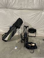 Wide shot of full lot showing golf bag with clubs, golf caddy, fishing pole with bait box, portable seat, and golf shoes with bag on concrete floor.
