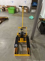 Full view of the yellow Harbor Freight ATV and Motorcycle Lift with black pedals and long handle on a concrete basement floor.
