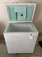 Open deep freezer showing white exterior and mint green interior lid and gasket with a central compartment molded inside.