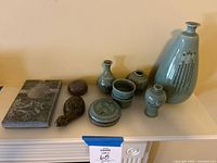 Seven-piece lot showing Korean pottery pieces in cerulean glaze, carved stone turtle, polished stone, and soapstone ashtray arranged on a shelf.