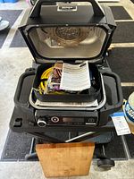 Top-down view of open Ninja Woodfire grill showing interior and accessories inside including hose and manual.