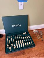 Original box with green exterior with Oneida branding, open to show neatly arranged tablespoons, knives, forks, and teaspoons with ornate Dover handle design.