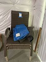 Stacked outdoor chairs with blue tarp on top, showing woven fabric and metal arms.