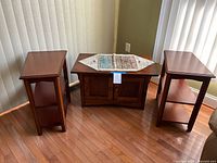 View of two end tables and one coffee table arranged on hardwood floor near window blinds.