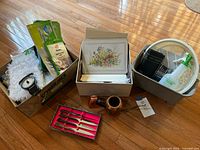 Photo showing box of cleaning supplies, floral greeting cards box, brown tobacco pipe, and set of 4 steak cutters in box.