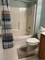 View of shower area with striped shower curtain, bathtub, and beige bath mat on tiled floor