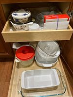 Drawer with assorted Corningware dishes and Pyrex baking dishes, including white ceramic casserole dishes with blue floral patterns, and glass dishes