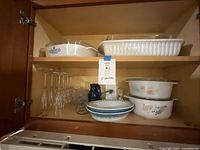 Cabinet shelf containing Pyrex baking dishes with lids, some serving bowls, and champagne glasses stored upright