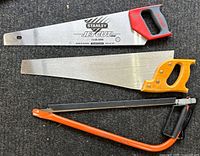 Top view of three saws on a grey surface: Stanley Jet Cut hand saw with red and black handle, traditional saw with yellow handle, and small orange frame hacksaw.