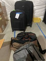 Two black Samsonite expandable rolling suitcases, larger and smaller size, front view showing front pouches and handles. Three small carry-on duffle bags are laid out in front.