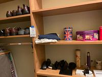 Shelving with multiple brown men's shoes on upper shelf, eyeglass cases, a kaleidoscope, Apple charging parts, and Magic Trackpad on lower shelves.