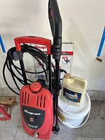 Front and top views of Snap-on red and black pressure washer with hose wrapped on handle, showing brand and pressure specs.