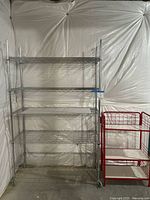 Full view of metal baker's rack and red shelving unit side by side in basement.