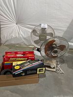 Lot contents including two articulated fans, furniture sliders, and tool kit in packaging.