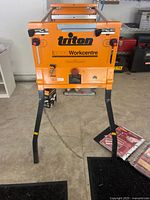 Front view of orange Triton 2000 Workcentre standing on foldable black metal legs with control knobs and labels visible.