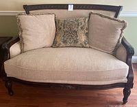 Front view of Victorian style beige upholstered loveseat with three decorative pillows (two beige with fringe, one patterned)