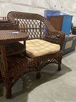 Wicker chair clearly showing the dark brown woven wicker structure with attached side table and seat cushion.