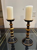 Pair of two black and gold metal candle sticks each with a white pillar candle on top.