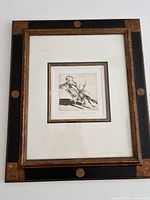 Framed engraving of seated man smoking a pipe. Black and gold decorative frame with white double mat.