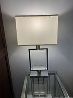 Full view of the rectangular table lamp with clear glass and metal base and white shade.