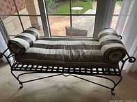 Front view of the black iron indoor bench with lattice seating platform, curved legs, and three striped cushions (one long seat cushion and two bolster cushions).