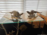 Pair of bronze pheasant figurines displayed on glass shelf with natural light.