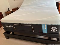 Side angle showing white mesh mattress cover with wavy pattern and grey side panel with Tempur-Pedic logo