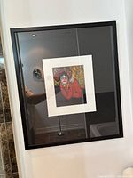 Framed Picasso print wall art showing a stylized portrait of a person in red with colorful background, behind glass in black frame.