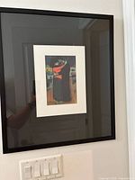 Framed Picasso print wall art hung on a white wall with light switches underneath. Image shows full frame and a part of room reflecting in the glass.