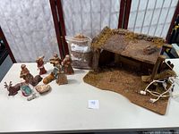 Porcelain bisque nativity figures and wooden stable arranged with light bulb and electric cord visible
