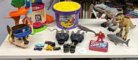Wide shot of assorted kids toys including dinosaurs, toy cars, kinetic sand, action figures, and playset.