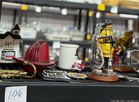 Firefighter statues in yellow uniform, red fire helmet magnet, brass hook, firehouse small plate, badge, and collectible fireman figurines.