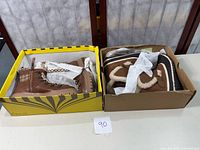 Two cardboard boxes containing two pairs of boots, one pair is brown lace-up and the other brown with zipper and faux fur lining, both size 7.