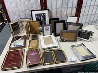 Photo showing the collection of 21 assorted picture frames arranged on a surface including brass, wood and metal frames.