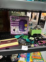 Photo showing Remington Paraffin Spa kit box, plastic hair accessories in green and black boxes, five pairs of colorful plastic sunglasses, and Buxton wallet box on a black surface.
