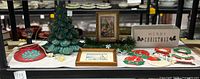 Full lot displayed on black shelf including ceramic Christmas tree, two wooden framed Christmas scenes, rectangular Merry Christmas box, door knob hangers, and small bulbs for tree lights.