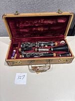 Open clarinet case showing disassembled black clarinet with silver keys, lined with burgundy velvet, with cork grease, reed, and a small key.