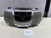 Front angle view of the Coby portable CD/cassette/radio recorder showing built-in stereo speakers on either side, central control panel with buttons for power, playback, and cassette functions.