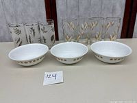 Three Corelle cereal bowls with gold butterfly pattern and two sets of Libbey drinking glasses, gold wheat rimmed and silver leaf pattern.