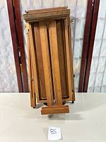 Folded wooden travel easel upright showing the adjustable wooden slats and supporting stand.
