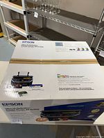 Sealed box of Epson Ultra Hi-Definition RX680 Photo printer showing front and top with branding and product details.