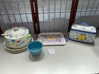 Photo shows three ceramic kitchenware items: covered serving bowl with floral design and ladle, small turquoise bowl, and rectangular bread box with lemon decoration and chipped lid.