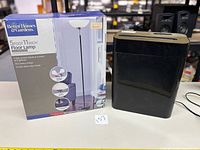 Photo of the unopened 5'11" Better Homes & Gardens black and brass floor lamp box next to the black paper shredder.