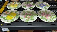 Six 8-inch ceramic plates arranged in two rows featuring different raised fruit designs and green leaves on a white background.