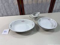 Set of 4 small bowls stacked beside a large serving bowl and creamer on a table